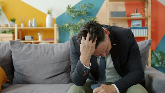 Man in suit sitting on couch with head in hands.